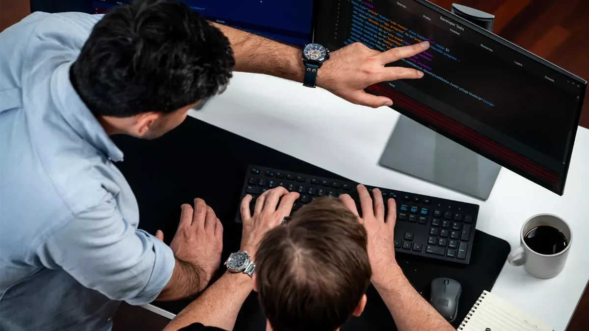Two local web developers reviewing code on a desktop monitor, discussing a website project in a collaborative workspace.